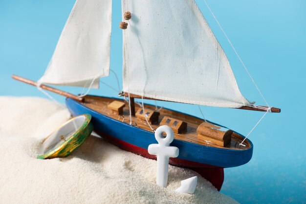 Miniature ship near compass and anchor in white sand isolated on blue