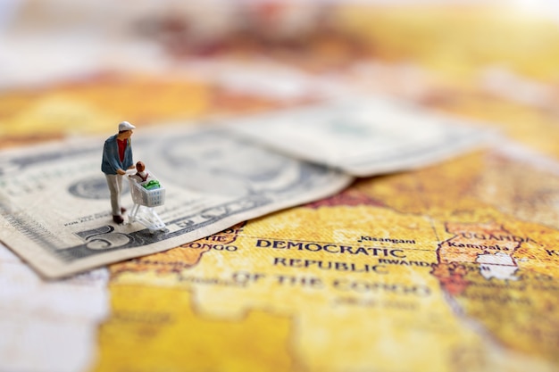 Miniature Shoppers with shopping cart standing on the  money and world map.