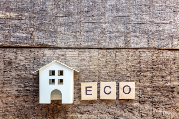 Miniature toy model house with inscription ECO letters word on wooden background