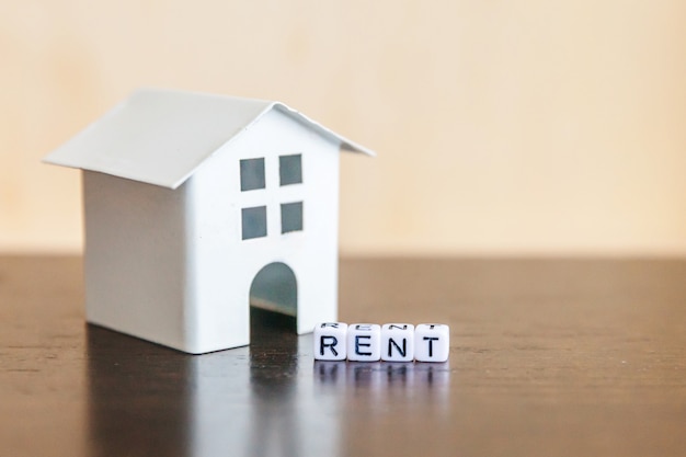 Photo miniature toy model house with inscription rent letters word on wooden backdrop. eco village, abstract environmental background. real estate mortgage property insurance sweet home ecology rent concept