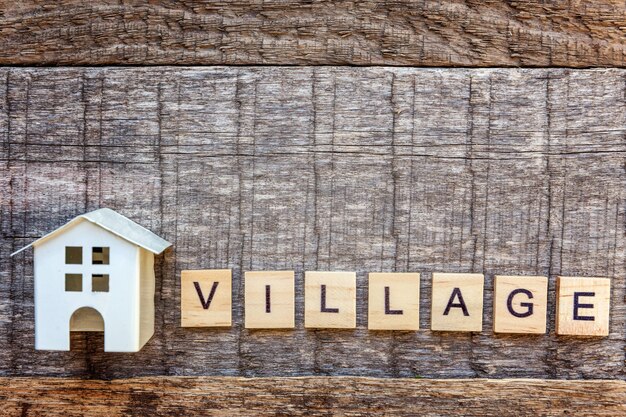 Miniature toy model house with inscription VILLAGE letters word on wooden background