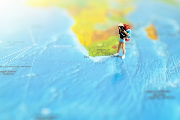 Miniature traveler with a backpack standing on world map. Travel concept.