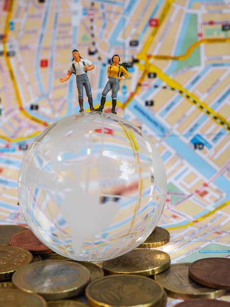 Foto viaggiatore o viaggiatore zaino in spalla in miniatura su globo di vetro, monete in euro e mappa.