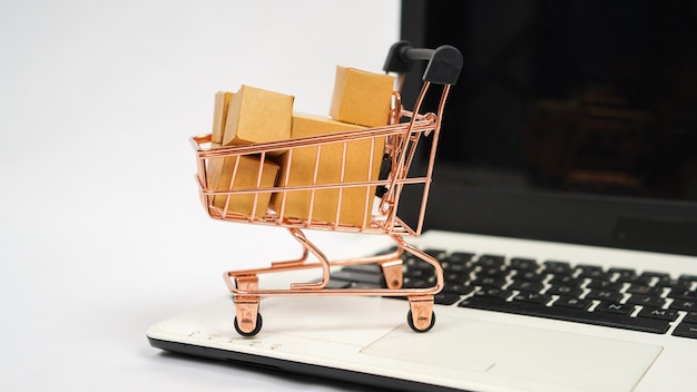 Miniature trolley filled with brown boxes and laptop isolated on white background