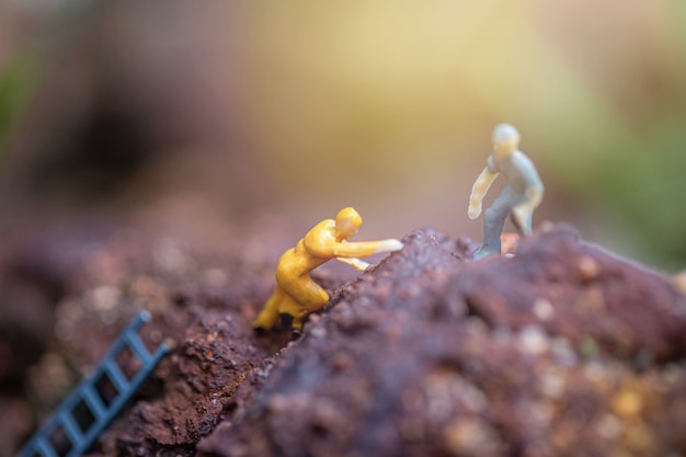 miniature of two friends helping each other to reach the top of the mountains