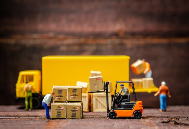 Miniature warehouse workers forklift carrying goods box to semi truck with trailer