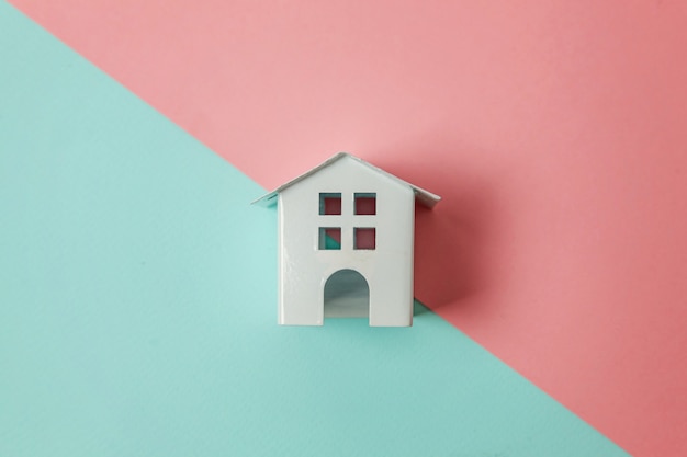 Miniature white toy house on blue and pink pastel background