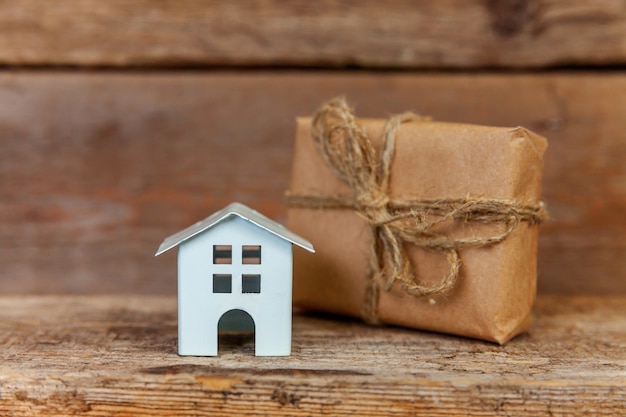 Photo miniature white toy house and gift box wrapped craft paper on old wooden background