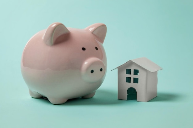 Miniature white toy house and piggy bank on blue background