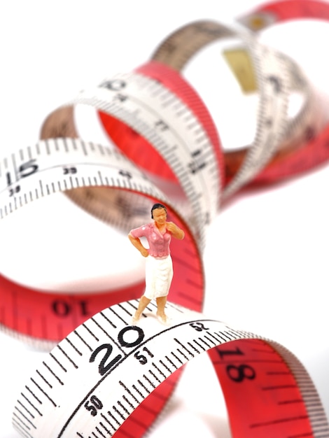 Miniature woman standing near measuring tape, thinking of weight loss and slim body.