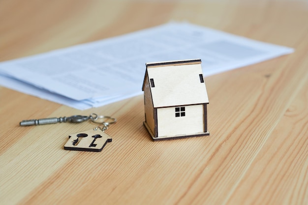 Miniature of a wooden house a metal key with a keychain a contract on a wooden table