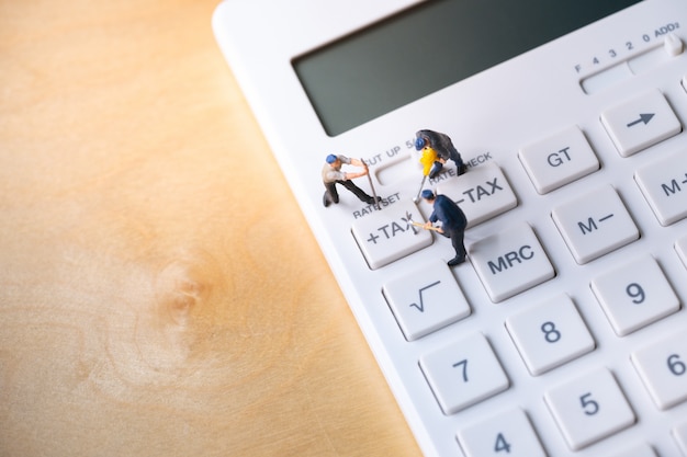 Photo miniature workers digging tax button on calculator