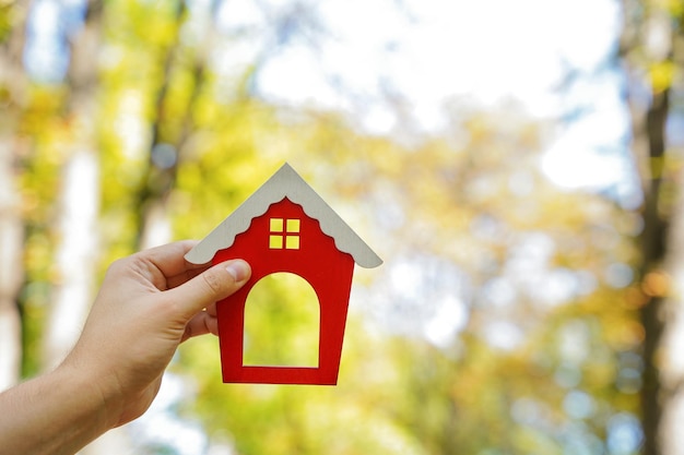 Miniatuur houten huis in de handen van een man buitenshuis vastgoedconcept ecovriendelijk huis een huis kopen buiten de stad rood dak selectieve focus