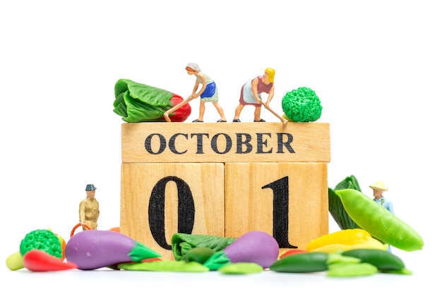 Miniatuur mensen landbouw bezig met hout kalender 1 oktober op witte achtergrond. wereld vegetarisch dag concept