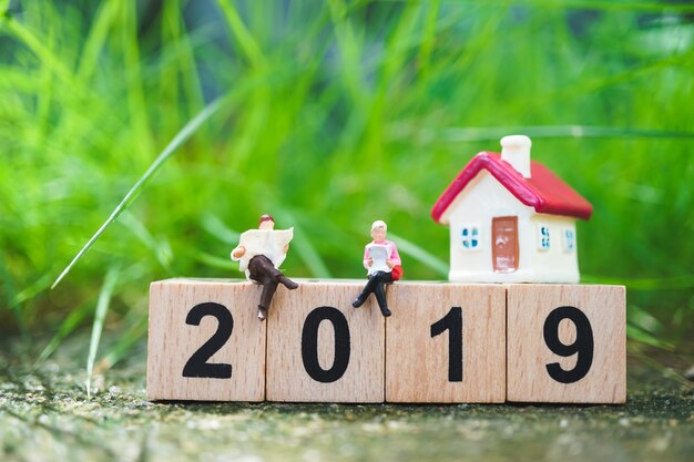 Miniatuur mensen, man en worman lezen op houten blok jaar 2019 met mini-huis