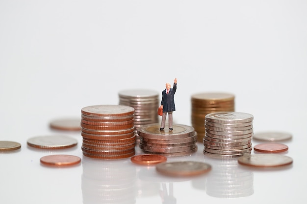 Miniatuur mensen: zakenman die zich op het stapelen van munten bevindt