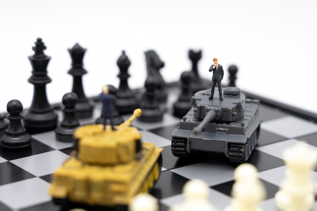 Miniatuur mensenzakenlieden die zich op een schaakbord met een tankmodel bevinden