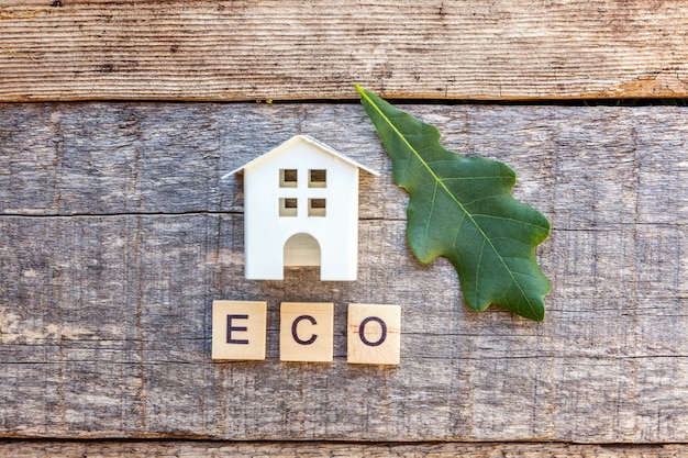 Foto miniatuur speelgoed modelhuis met inscriptie eco letters woord op houten achtergrond