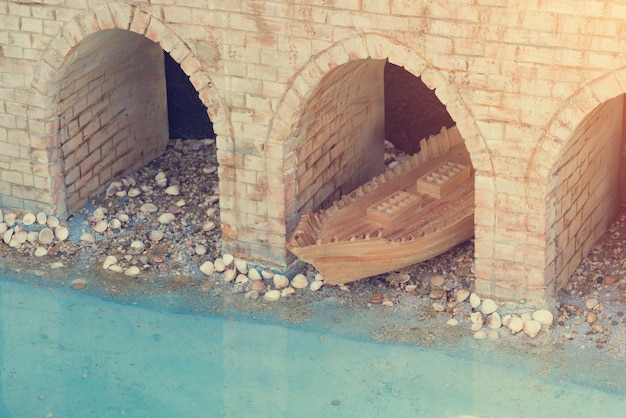 Miniatuurbakstenen muur met bogen en houten stuk speelgoed boot dichtbij water