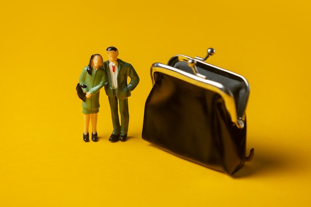 Miniatuurfiguren van een man en vrouw naast klassieke portemonnee op gele ondergrond