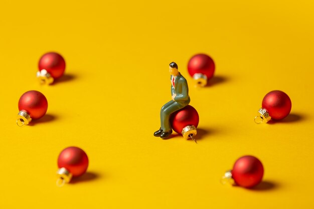 Miniatuurfiguur van man zit op kerstbal op gele ondergrond