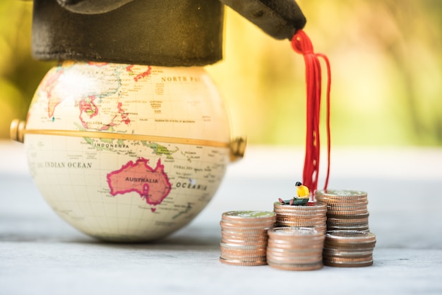 Foto miniatuurmensen die en op muntstukkenstapel zitten lezen voor een bol met afstuderenhoed. financieel en onderwijs.