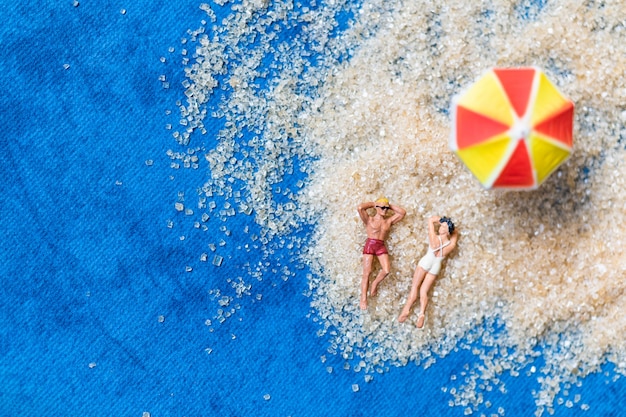 Miniatuurmensen die op het strand zonnebaden, het concept van de de Zomertijd