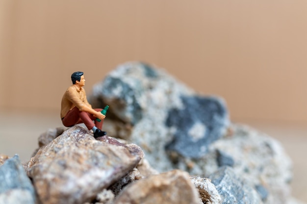 Miniatuurmensen Een jonge man drinkt bier terwijl hij op de rots zit