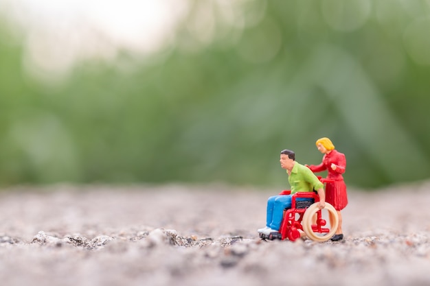 Miniatuurmensen: gehandicapte mensenzitting in rolstoel in het park en exemplaarruimte voor tekst