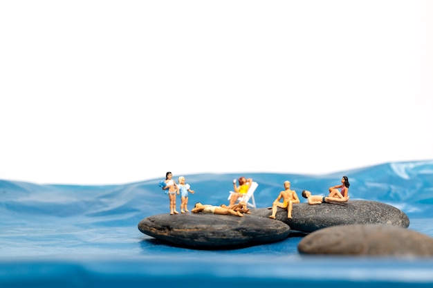 Miniatuurmensen, gelukkige familie zittend op de grote rotsen bij de kust met blauwe zee en witte achtergrond, zomerconcept