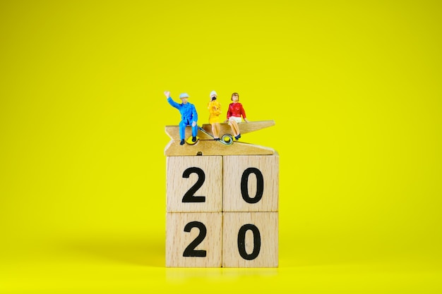 Miniatuurmensen, man en vrouw die op houten blok 2020 zitten als zakelijk en sociaal concept te gebruiken