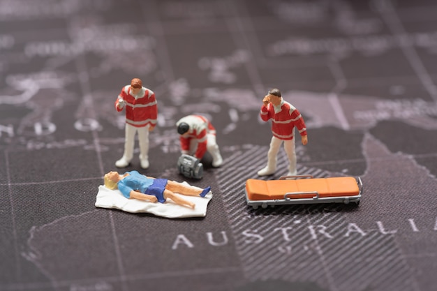 Foto miniatuurmensen, noodsituatie medisch team op het werk bij ongevallenscène op wereldkaart.