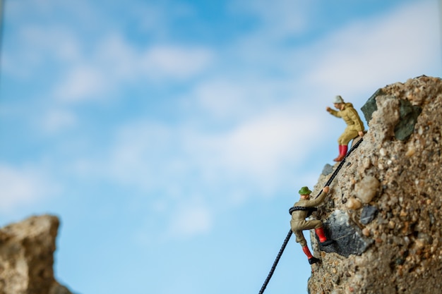 Miniatuurmensen: wandelaars die op de rots klimmen. Sport en recreatie concept.