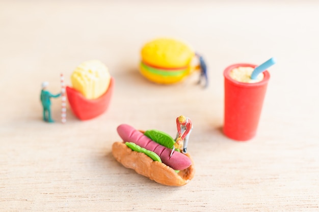 Miniatuurmensenarbeiders maken hotdogbroodjes, fastfood en junkfoodconcept.