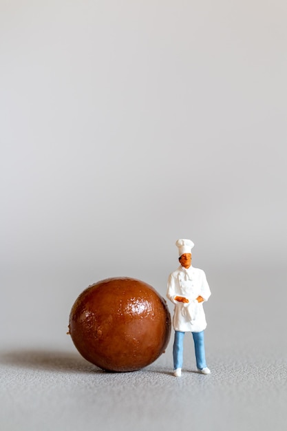 Miniatuurmensenchef-kok met chocolade die zich bevindt terwijl hij tegen een grijze achtergrond staat