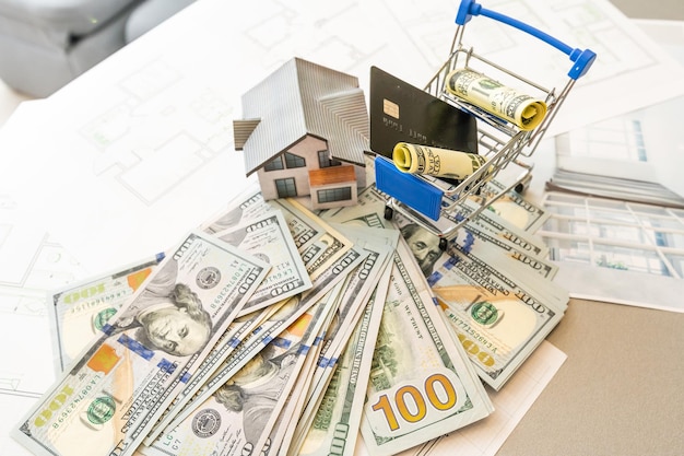 Miniatuurmodel van huis tegen de achtergrond van een huisplan, en geld, en rekenmachine.