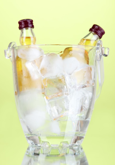 Minibar bottles in bucket with ice cubes on color background