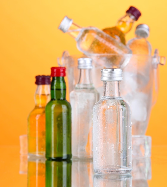 Minibar bottles in bucket with ice cubes on color background