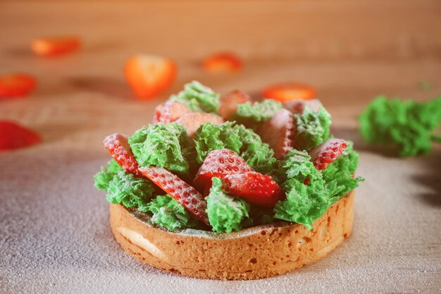 Minicake met plakjes aardbei, greens en room op koekje met poedersuiker