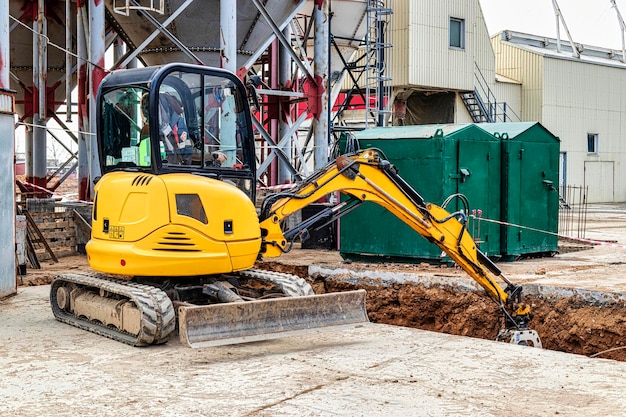 Minigraafmachine graaft een greppel op een bouwplaats Leggen van ondergrondse rioolbuizen en communicatie tijdens de bouw Compact bouwmaterieel Grondwerken uitgraven