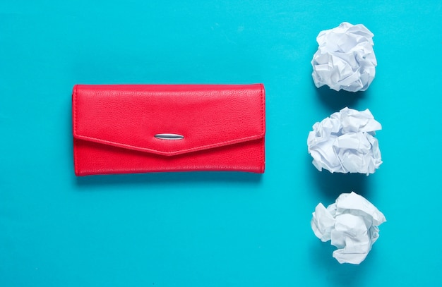 Minimaal concept. Verfrommeld papier ballen, rood lederen portemonnee op blauwe tafel