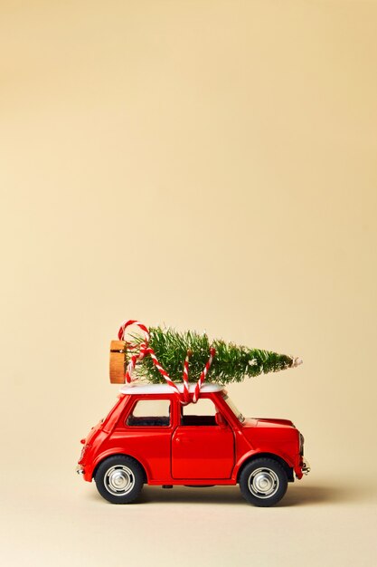 Minimaal ontwerp voor het vieren van kerst- of nieuwjaarswenskaart. Cadeau levering concept. Kleine rode speelgoedauto en kerstboom op een lichte achtergrond