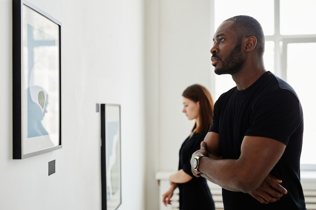 Minimaal zijaanzichtportret van een Afro-Amerikaanse man die naar schilderijen in een moderne kunstgalerie kijkt, kopieer ruimte