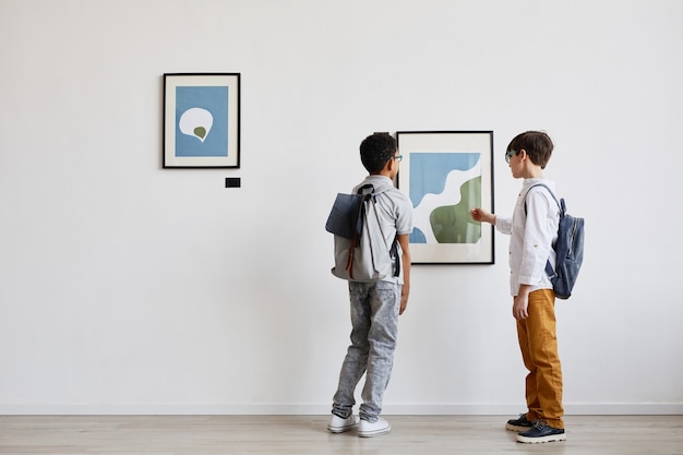 Minimal back view portrait of two schoolboys looking at abstract paintings in modern art gallery, copy space