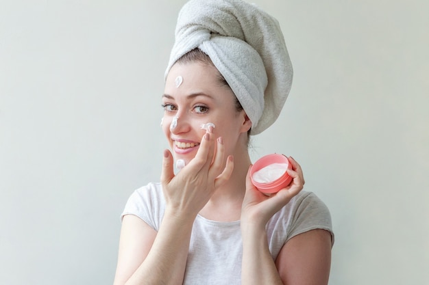 Minimal beauty woman girl in towel on head portrait applying white nourishing mask or creme on face isolated on white background.