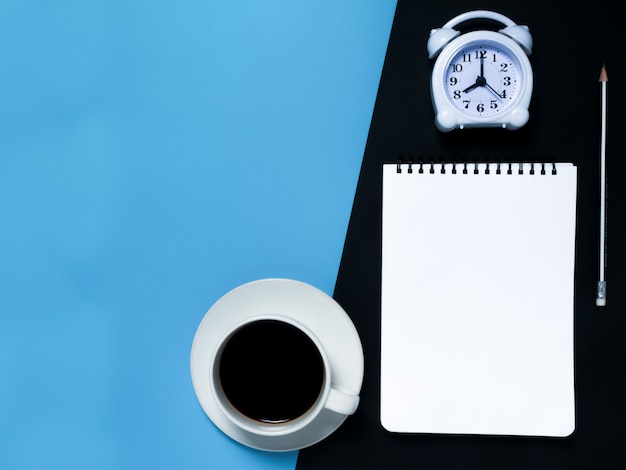 Minimal black work space concept : Notepad , pencil , alarm clock, coffee, top view.