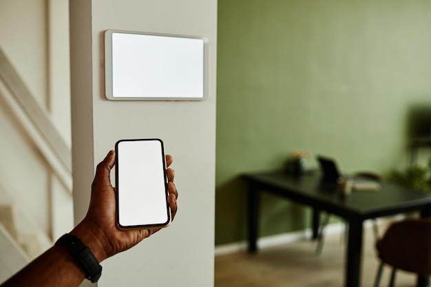 Minimal close up African American man holding phone with blank screen while connecting to smart home system copy space