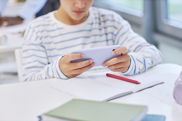 スマートフォンを持ち、学校でモバイルゲームをする子供の最小限の接写