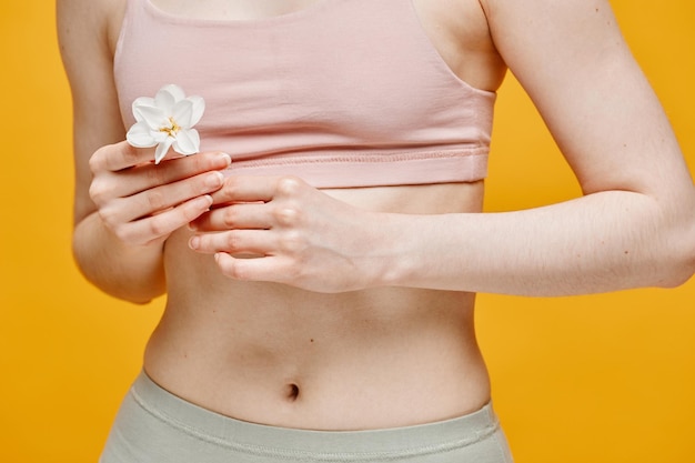 Minimal close up of unrecognizable young woman wearing underwear with flower against vibrant yellow