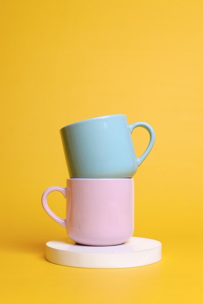 Minimal composition of ceramic mugs stacked on round shaped podium against yellow background